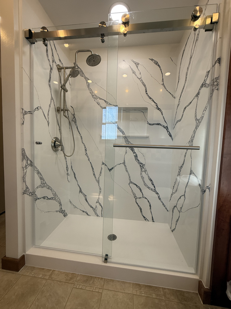 Full view of a marble-look shower with frameless glass door and rain showerhead installed by Righteous Renovations in Salem, OR