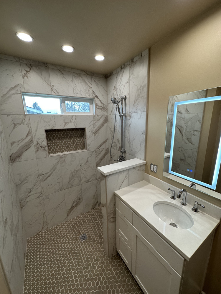 Modern walk-in shower with partial wall divider and marble-look tile by Righteous Renovations in Salem, OR