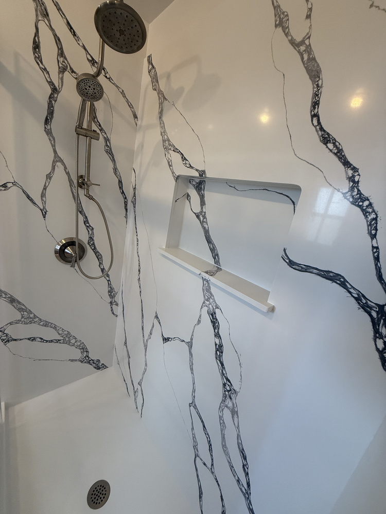 Angled view of a luxury shower with veined panel walls and brushed nickel shower system by Righteous Renovations in Salem, Oregon