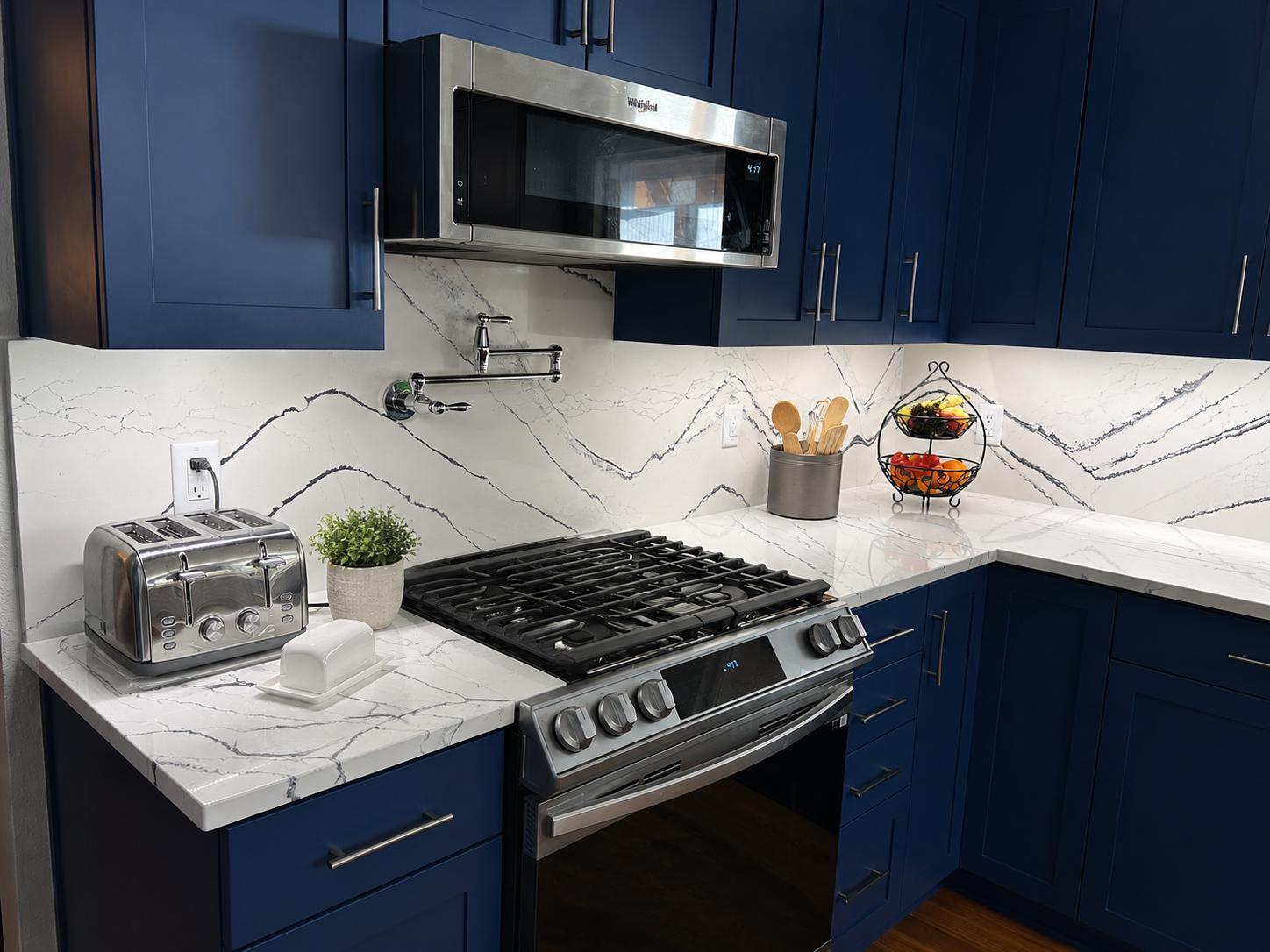 Modern navy blue kitchen with stainless steel appliances and marble-look countertops by Righteous Renovations in Salem, OR