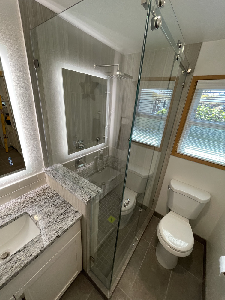 Full bathroom view with granite vanity, walk-in shower, and window lighting by Righteous Renovations in Salem, Oregon