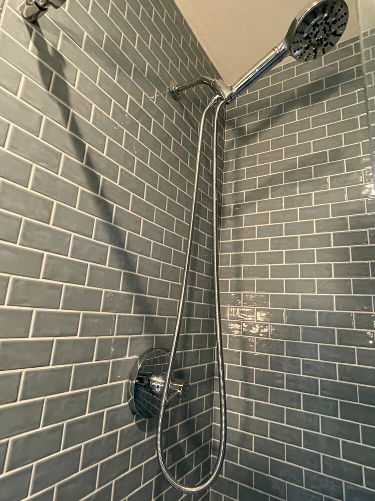 Detail of tiled shower wall with modern handheld showerhead installed by Righteous Renovations in a Salem, Oregon custom home