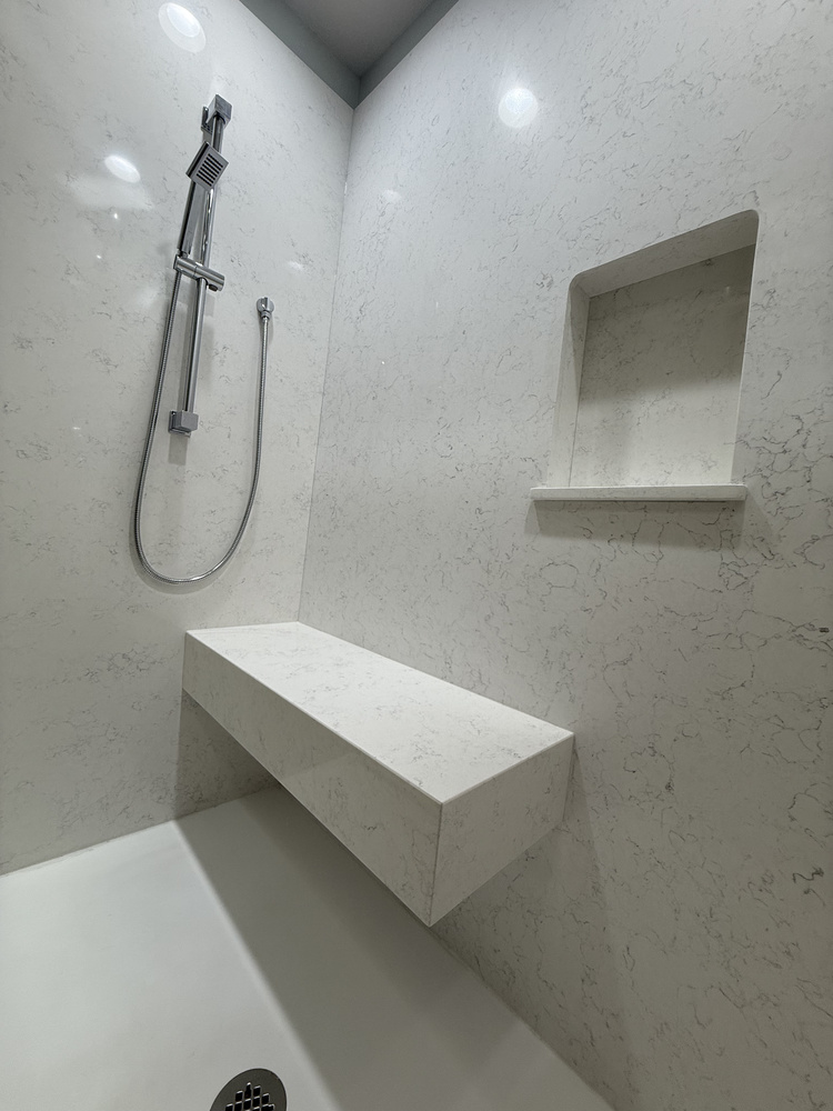 Corner view of a walk-in shower with marble-look walls and built-in bench in a Salem, OR home by Righteous Renovations