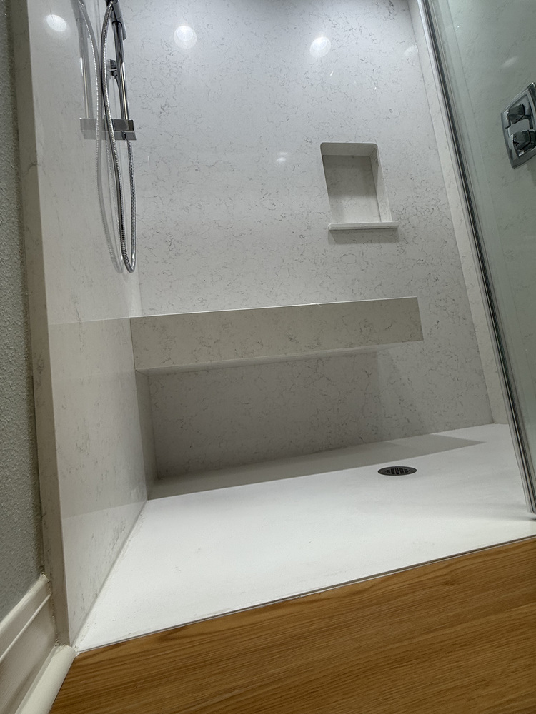 Side view of a modern shower with chrome hand-held sprayer and built-in shelf in a Righteous Renovations project